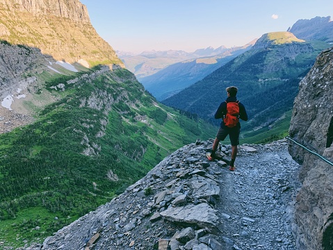 A hiker and backpacker takes in the beautiful view along the Highline Trail during an early morning hike. Image taken at Glacier National Park, Montana, USA.