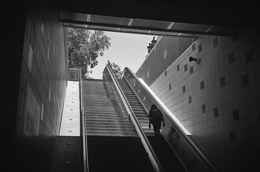 An upward leading set of stairs / escalator, with a dark figure making its way toward the light, away from the darkness and shadows