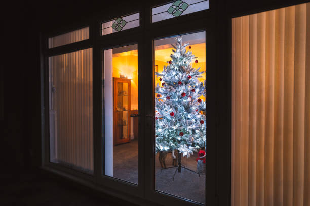 istock A frosted white artificial christmas tree with red and silver decorations seen through large patio doors with vertical slat blinds and bevel window designs. 1192360706