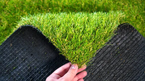Photo of Hand holding an artificial grass roll. Greenering with an artificial turf.