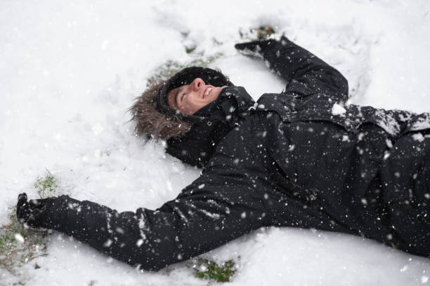 istock Young man laughing, with happy expression, snow covered, lying on the ground in snowfall. 1192363922