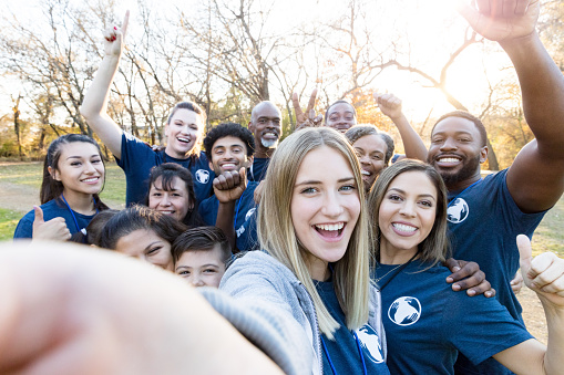 Young woman takes a selfie with a group of friends who are participating in a community cleanup event.