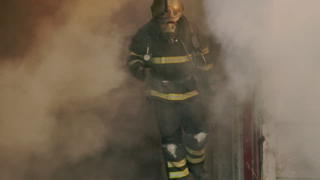Slow motion fire fighter running towards the camera with fire in the background.