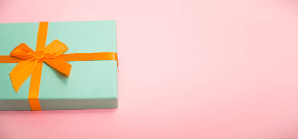 istock green box with gifts with an orange bow on a pink 1192382782