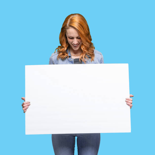 one person / waist up / front view / looking down of 20-29 years old adult beautiful redhead / long hair caucasian female / young women standing wearing jeans / pants / double denim / denim jacket who is smiling / happy / cheerful / laughing - one young woman only only young women one woman only 20 25 years imagens e fotografias de stock