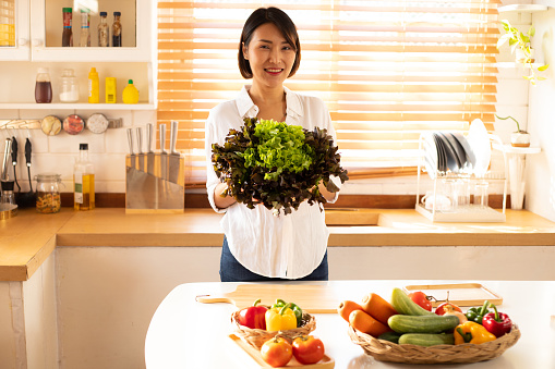 Asian woman in a kitchen cutting vegetables and preparing healthy meal Kitchen at home