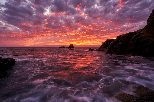 A very high tide coincides with a fiery sunset as the waves roil at Crescent Bay, Laguna Beach California