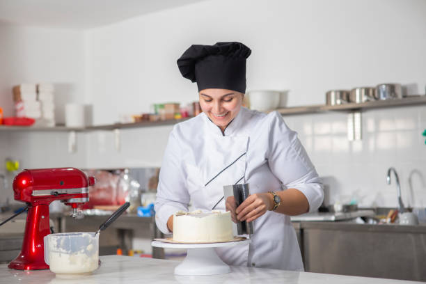 joven chef pastelera o una panadera preparando un pastel. - cake women confectioner photography fotografías e imágenes de stock