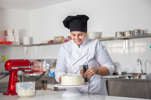 Young female pastry chef or a baker preparing a cake.