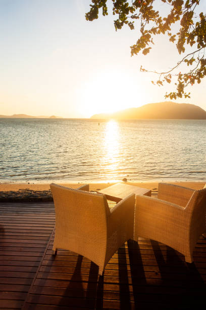 istock Table and chairs on wooden decking at early sunrise by seaside, vertical composition 1192403745