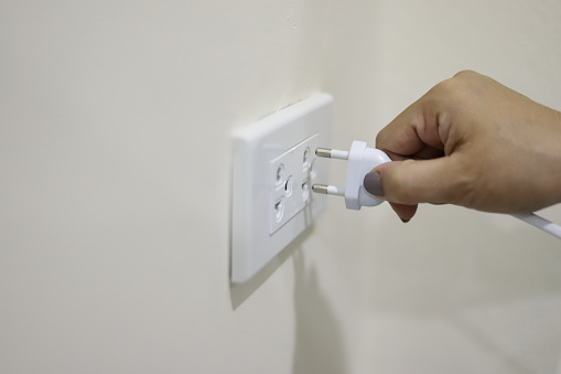 Woman's hand about to plug an electrical plug into an outlet