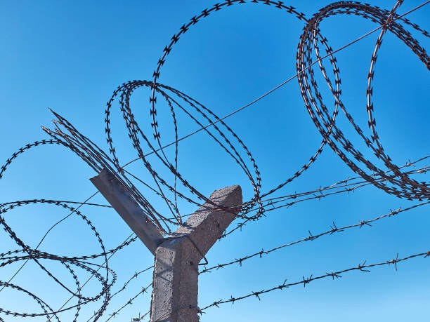 istock Barbed wire on fence opposite clear blue sky 1192425379