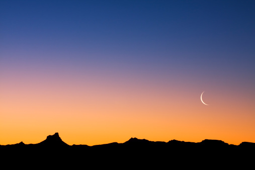 Moonrise Over Red Rock Canyon and Mountains - Scenic view with full moon, blue sky and orange/red rock warmly lit at sunset. Moon in lower third of sky with copy space.
