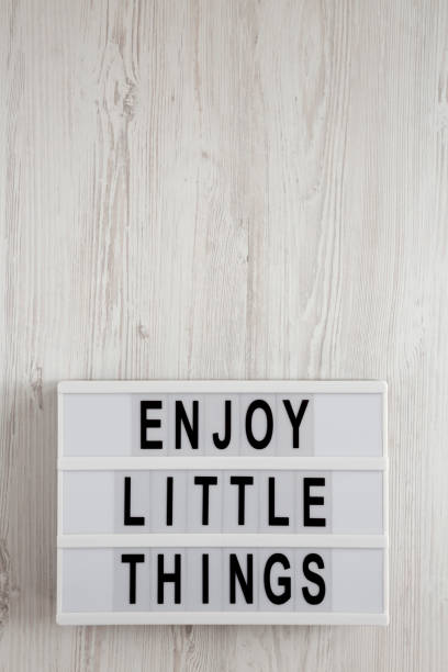 istock 'Enjoy little things' words on a lightbox on a white wooden surface, top view. Overhead, from above, flat lay. Copy space. 1192440022