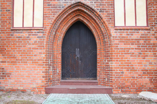 Weathered door with a unique iron handle against a rustic brick wall showcases fine craftsmanship.