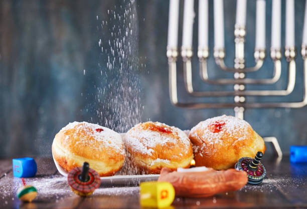 유대인 휴일 하누카 배경입니다. 전통 요리는 달콤한 도넛입니다. 하누카 테이블은 파란색 배경에 촛불과 회전 상판으로 촛대를 설정합니다. 가루 설탕과 도넛을 뿌린다. 복사 공간 - menorah hanukkah israel judaism 뉴스 사진 이미지