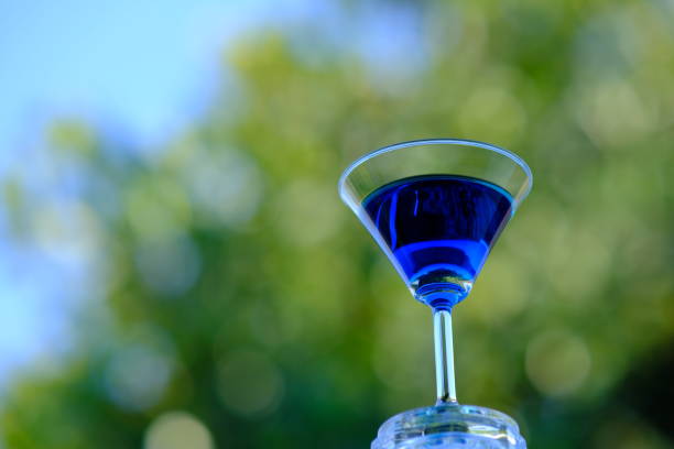 A glass of whiskey straight-up on a reflective surface against a blue background in studio.