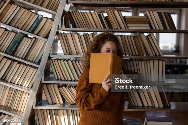 Young Woman Reading A Book In Apartment Stock Photo - Download Image Now - Book, Bookshelf, Laughing