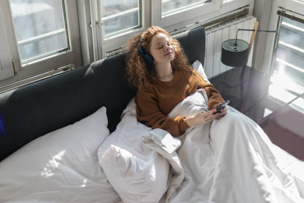 istock Young woman sitting on bed and using mobile phone 1192472441