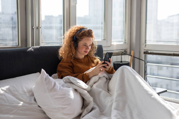 istock Young woman sitting on bed and using mobile phone 1192472671