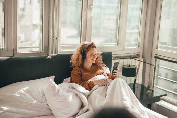istock Young woman sitting on bed and using mobile phone 1192472727