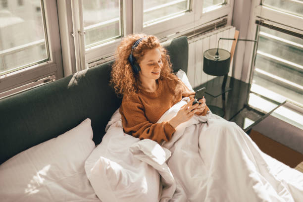 istock Young woman sitting on bed and using mobile phone 1192473141