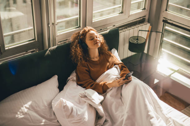 Young woman sitting on bed and using mobile phone