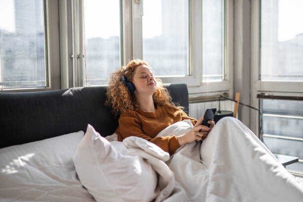 istock Young woman sitting on bed and using mobile phone 1192475165