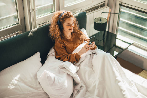 istock Young woman sitting on bed and using mobile phone 1192475271