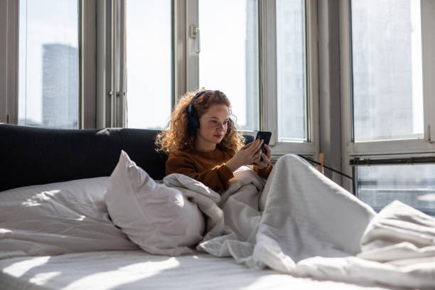 istock Young woman sitting on bed and using mobile phone 1192476507
