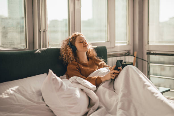 istock Young woman sitting on bed and using mobile phone 1192476558