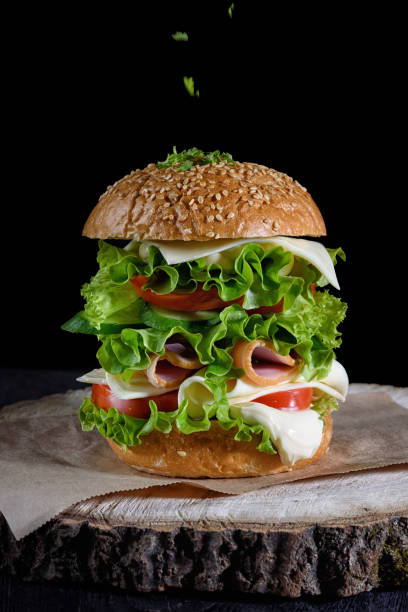 istock Big hamburger with ham, cheese, tomatoes and herbs on a black background 1192479560