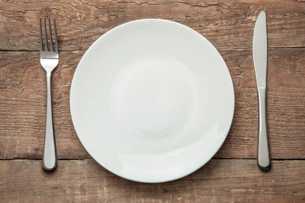 istock Empty white plate with knife and fork on a wooden table 1192479841