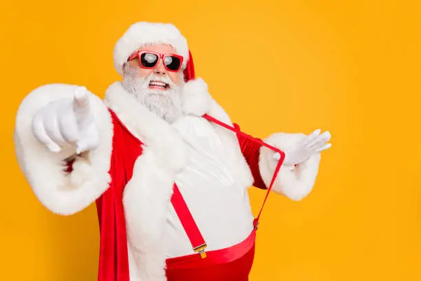 Profile side photo of funky fat santa claus point index finger choose, who will party with him on x-mas celebration pull stylish suspender isolated over yellow color background