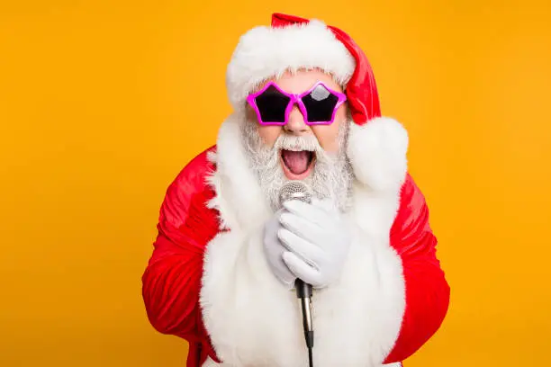 Jolly christmas x-mas performance from funky santa claus. Modern crazy grandfather in red fairy north-pole creature costume, sing song on stage hold microphone scream isolated yellow color background