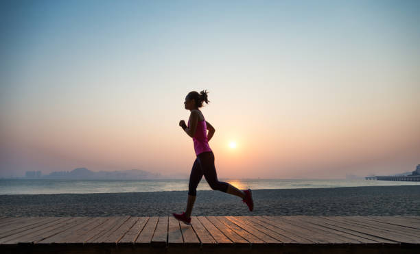 silhouette de jeune femme faisant le jogging sur le rivage au lever de soleil - running jogging asian ethnicity women photos et images de collection