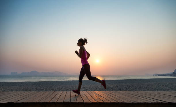 silhouette di giovane donna che fa jogging a terra all'alba - running jogging asian ethnicity women foto e immagini stock