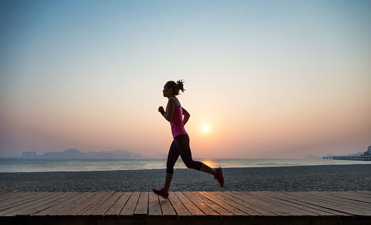 Silhouette of young woman jogging on shore at sunrise