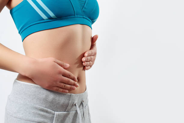 le concept de grossesse précoce, une bonne nutrition, la santé des femmes. photo de plan rapproché d'un beau ventre mince et d'un nombril d'une femme. elle touche les deux paumes de ses mains à sa taille - beautiful the human body body care close up photos et images de collection