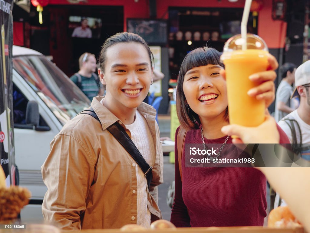 Young Couple Enjoying Food Truck Life in Khao San Road. Bangkok, Young asian couple fun spending time in Khao San Road. They buying juice, enjoying various kinds of street food. Smoothie Stock Photo