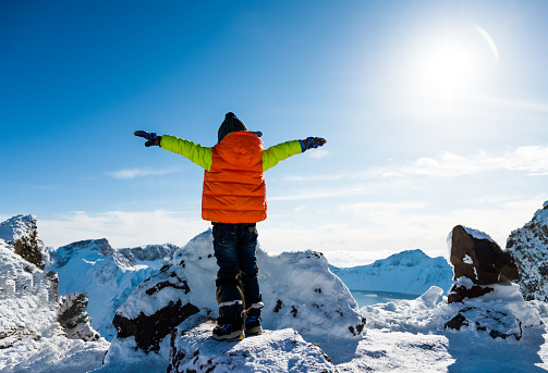Young boy lifts his arms on the top of snow mountains.