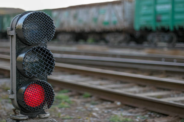 Semaphore with a glowing red lamp close-up. Selective focus on the semaphore. Background with rails and wagons blurred.