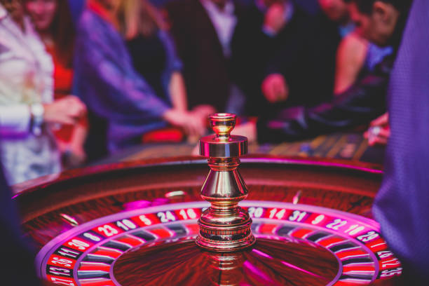 A close-up vibrant image of multicolored casino table with roulette in motion, with casino chips. the hand of croupier, mone and a group of gambling rich wealthy people in the background A close-up vibrant image of multicolored casino table with roulette in motion, with casino chips. the hand of croupier, mone and a group of gambling rich wealthy people in the background"n roulette photos stock pictures, royalty-free photos & images