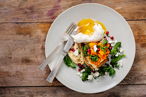 Overhead view of a dish of; grilled kale leaves, mashed pumpkin, pomegranate seeds and a poached egg on a piece of toasted granary bread. Colour, horizontal with some copy space.
