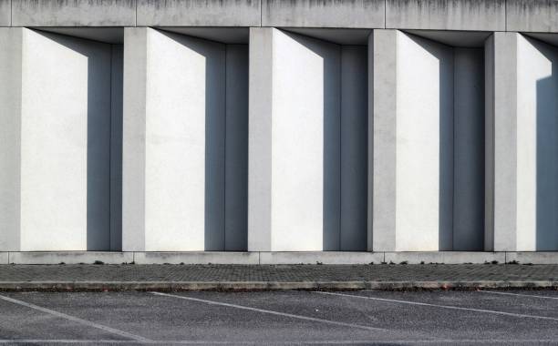 White concrete wall with long vertical shadows in the indentations. Sidewalk and asphalt street in front