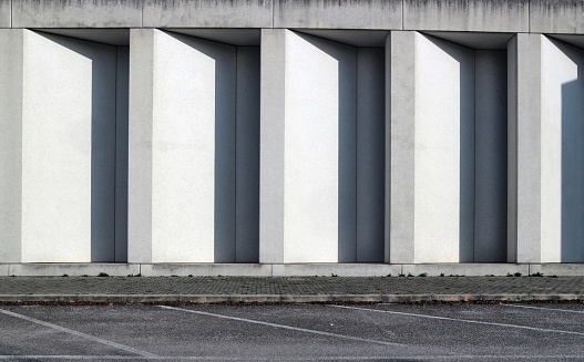 White concrete wall with long vertical shadows in the indentations. Sidewalk and asphalt street in front, background and texture for copy space