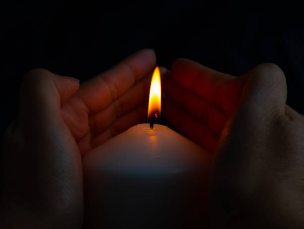 istock Hand protecting candle light from the wind in darkness on black background 1192510435