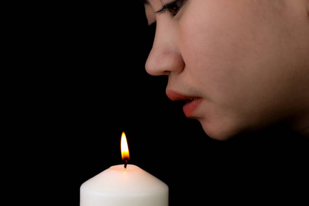 Young woman blowing a candle flame at black background