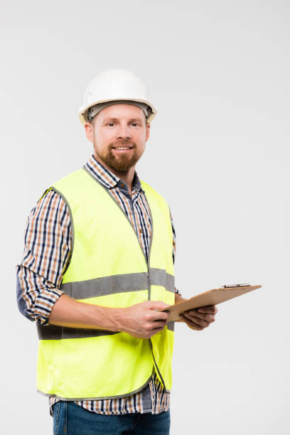 alegre capataz joven o ingeniero con portapapeles de pie en aislamiento - inspector safety construction reflective clothing fotografías e imágenes de stock