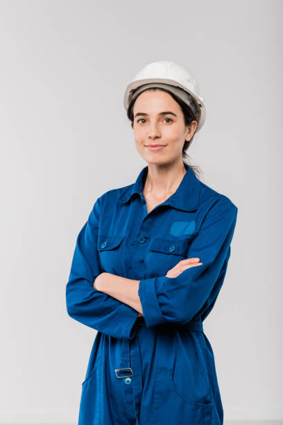 pretty young cross-armed female engineer in blue workwear and safety helmet - industrial objects imagens e fotografias de stock